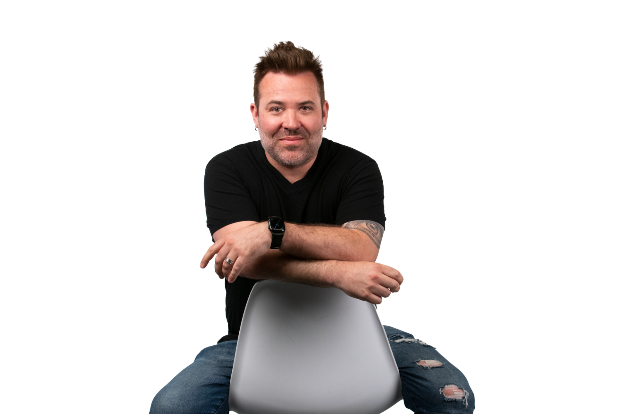 Brian West seated on a chair, wearing a black shirt and jeans